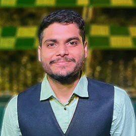 A smiling man wearing a green shirt and navy waistcoat stands in front of a chequered lime green background.